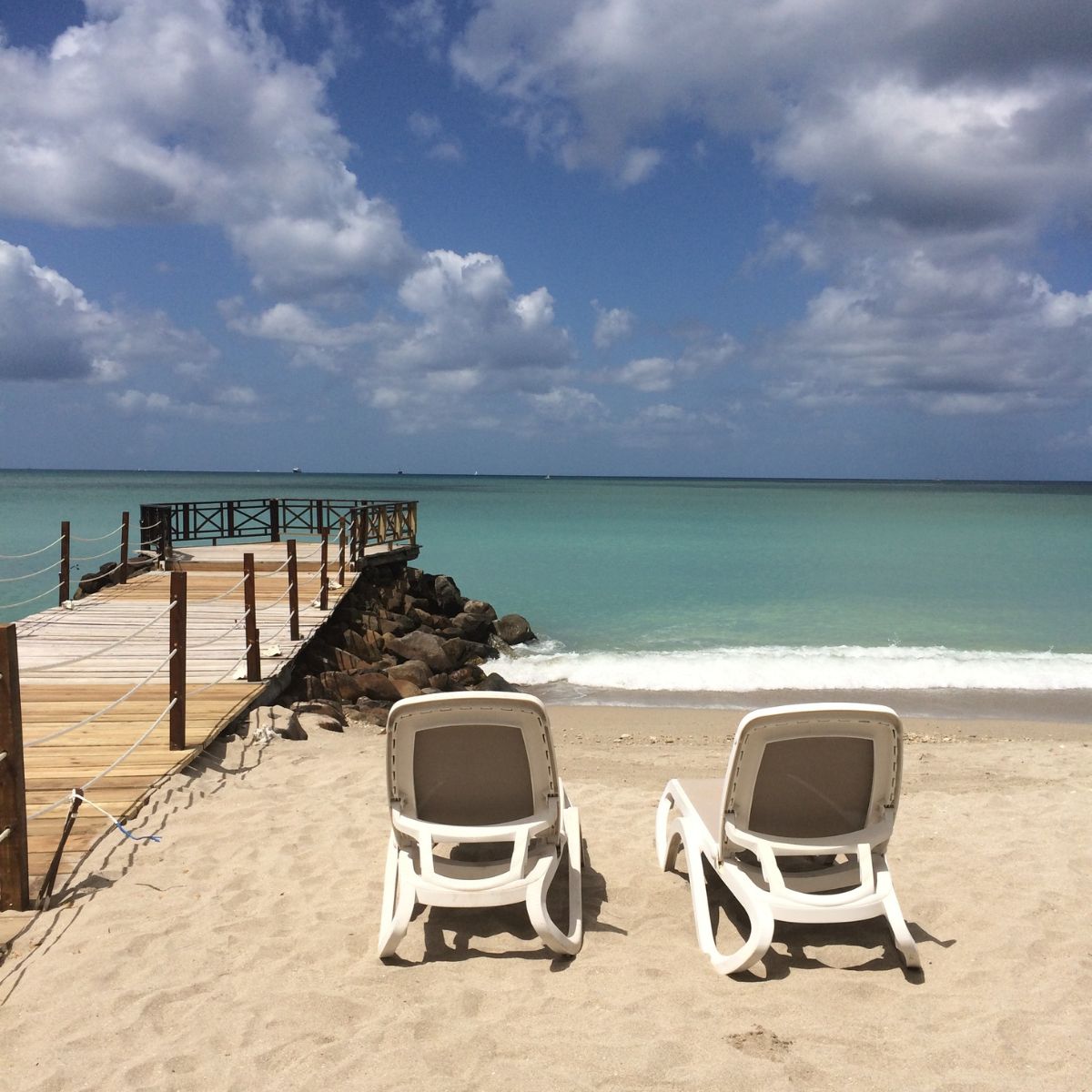 two chairs on a beach by a jetty