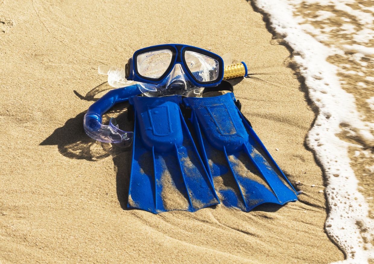 A pair of blue scuba goggles laying on the sandy beach during a St. Lucia vacation.