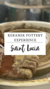 Hands deftly shaping clay on a pottery wheel with a sign reading "Keramik Pottery Experience, Saint Lucia," where artistry meets tradition.