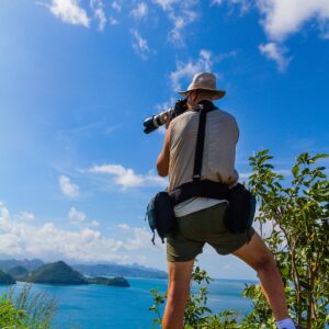 A person with a camera captures the stunning scenic view of the ocean and hills under a clear blue sky, reminiscent of St Lucia's breathtaking hiking trails.