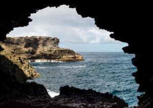 Gaze at the magnificent view of the ocean and rocky cliffs through the dark entrance of a cave, with cloudy skies above—a hidden gem among the things to do in Barbados.