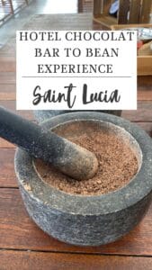 Mortar and pestle filled with crushed cocoa beans sit on a wooden table under a sign that reads "Hotel Chocolat Bar to Bean Experience Saint Lucia," offering a tantalizing glimpse into the St. Lucia chocolate tour experience.