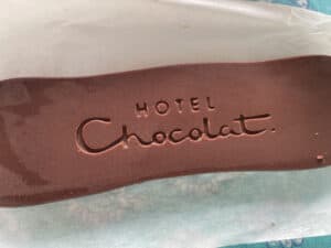 A rectangular piece of chocolate embossed with the words "Hotel Chocolat" lies on white parchment paper, reminiscent of a luxurious find from a St. Lucia chocolate tour.