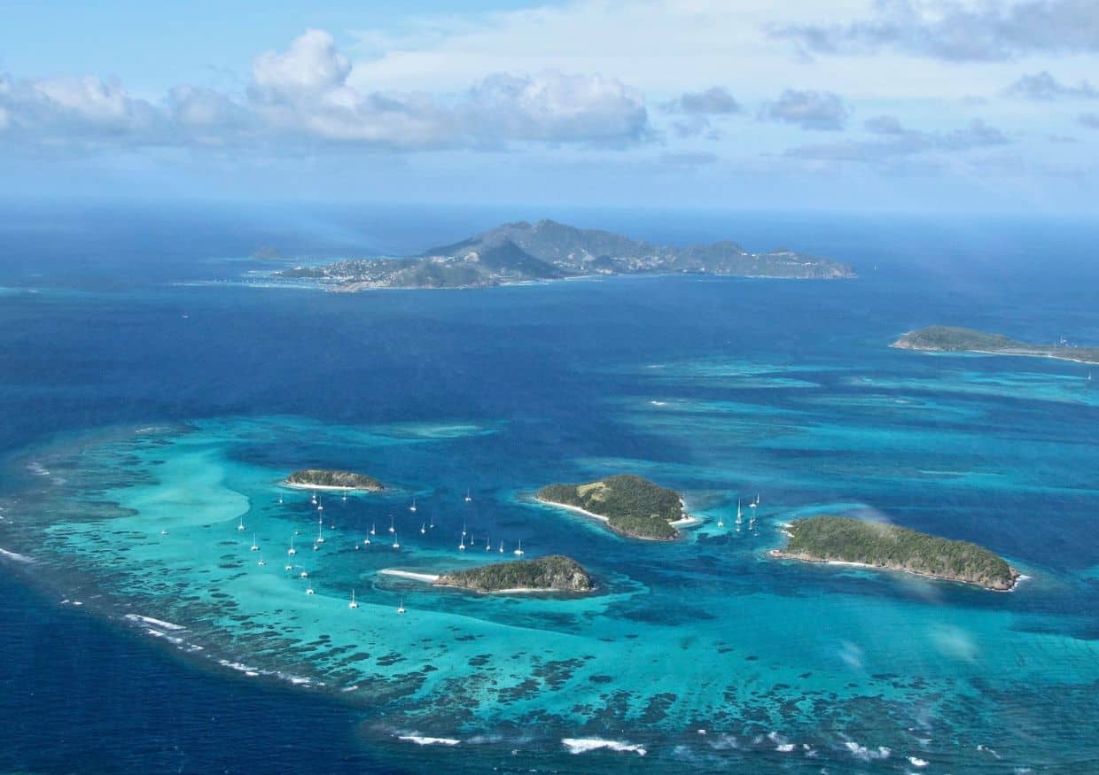 Aerial view of tropical islands close to St. Lucia, surrounded by turquoise water and several sailboats, with a larger island visible in the background under a partly cloudy sky.