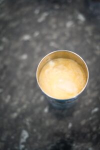 A stainless steel cup filled with a yellowish liquid placed on a speckled gray surface.