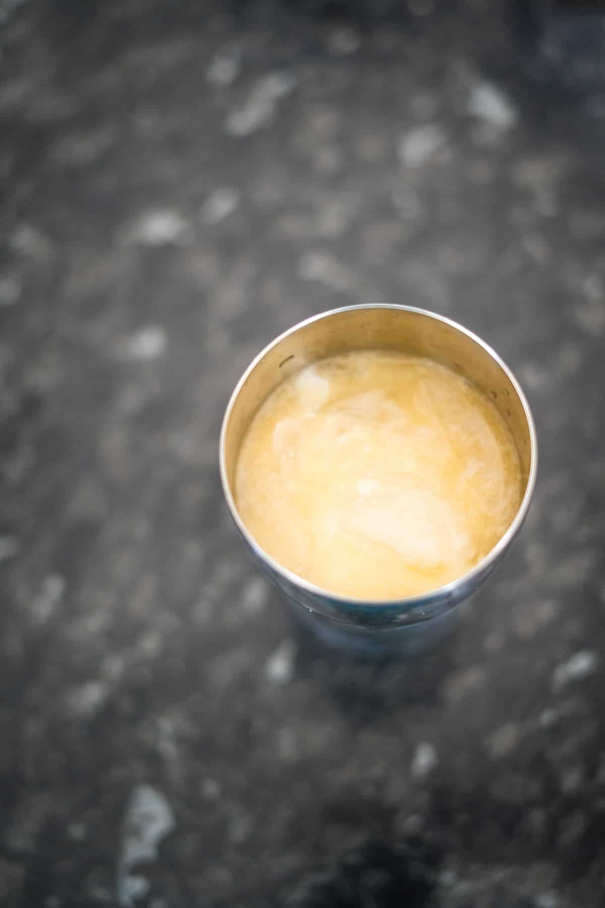A stainless steel cup filled with a yellowish liquid placed on a speckled gray surface.