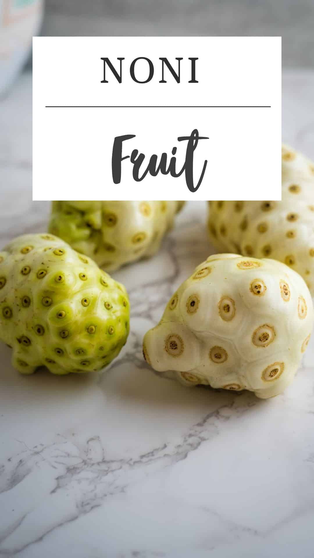 Four noni fruits on a marble surface with a label above saying "Noni Fruit.