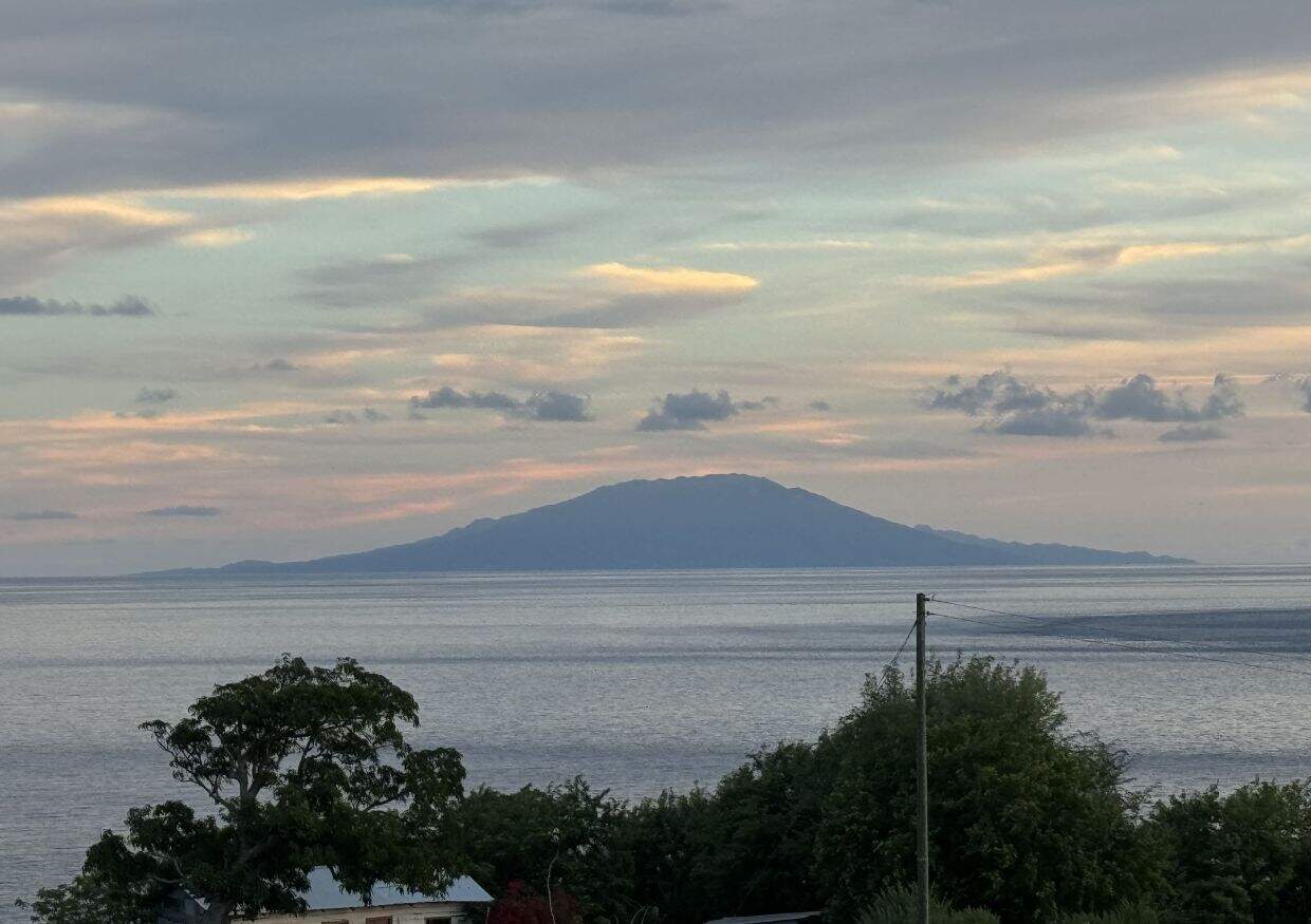 Distant view of an island near St. Lucia at sunset, with a calm sea in the foreground and trees silhouetted against the horizon.