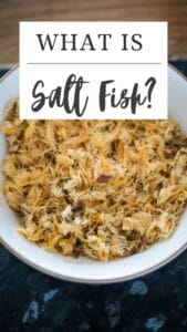 A bowl of shredded salt fish sits on a dark surface, with text elegantly asking, "What is Saltfish?.