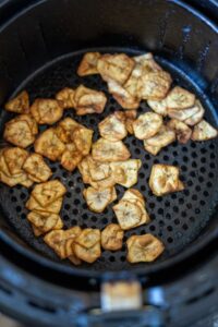 Slices of fried plantains mingle with crispy green banana chips in an air fryer basket.