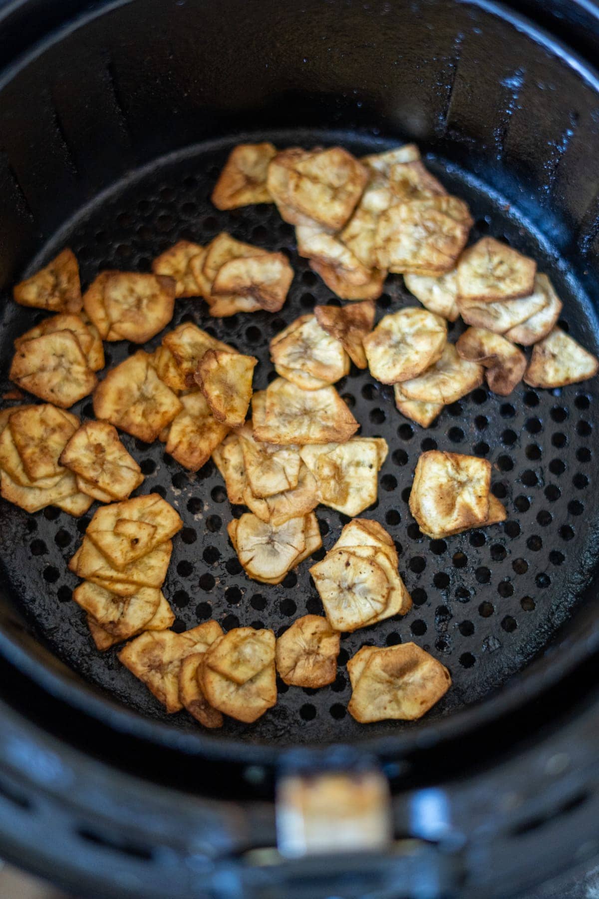 Slices of fried plantains mingle with crispy green banana chips in an air fryer basket.
