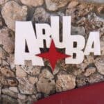Text "Aruba" in white with a red star, mounted on a stone wall background.