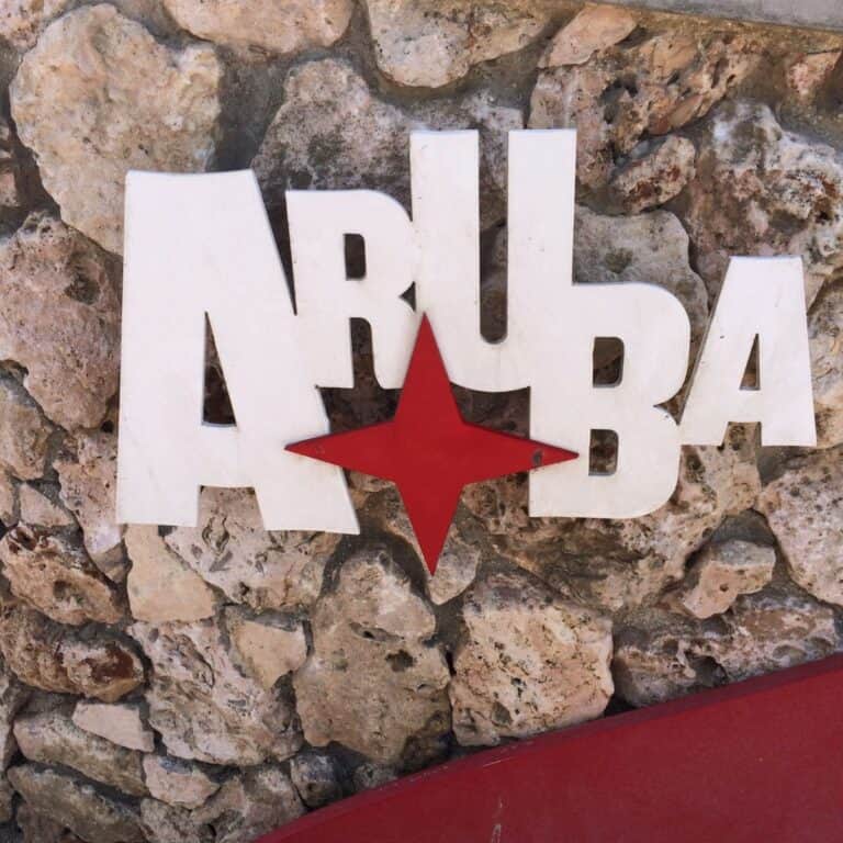 Text "Aruba" in white with a red star, mounted on a stone wall background.