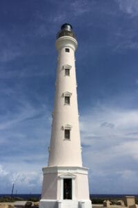 White lighthouse with multiple windows against a blue sky. A person is visible at the base entrance.