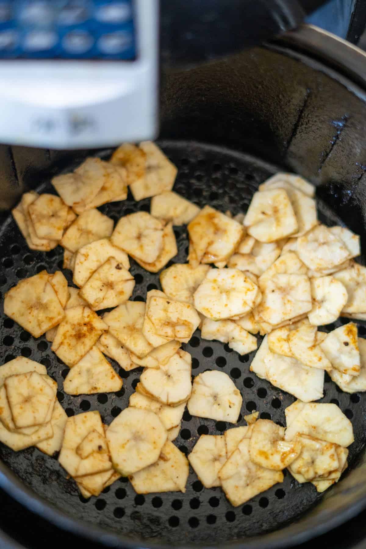 Slices of jicama, seasoned and mingling with green banana chips, sit nestled in an air fryer basket, ready for cooking.