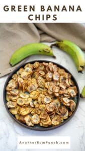 Plate of crispy green banana chips with whole green bananas in the background on a marble surface. Text above reads "Green Banana Chips." Website URL at the bottom.