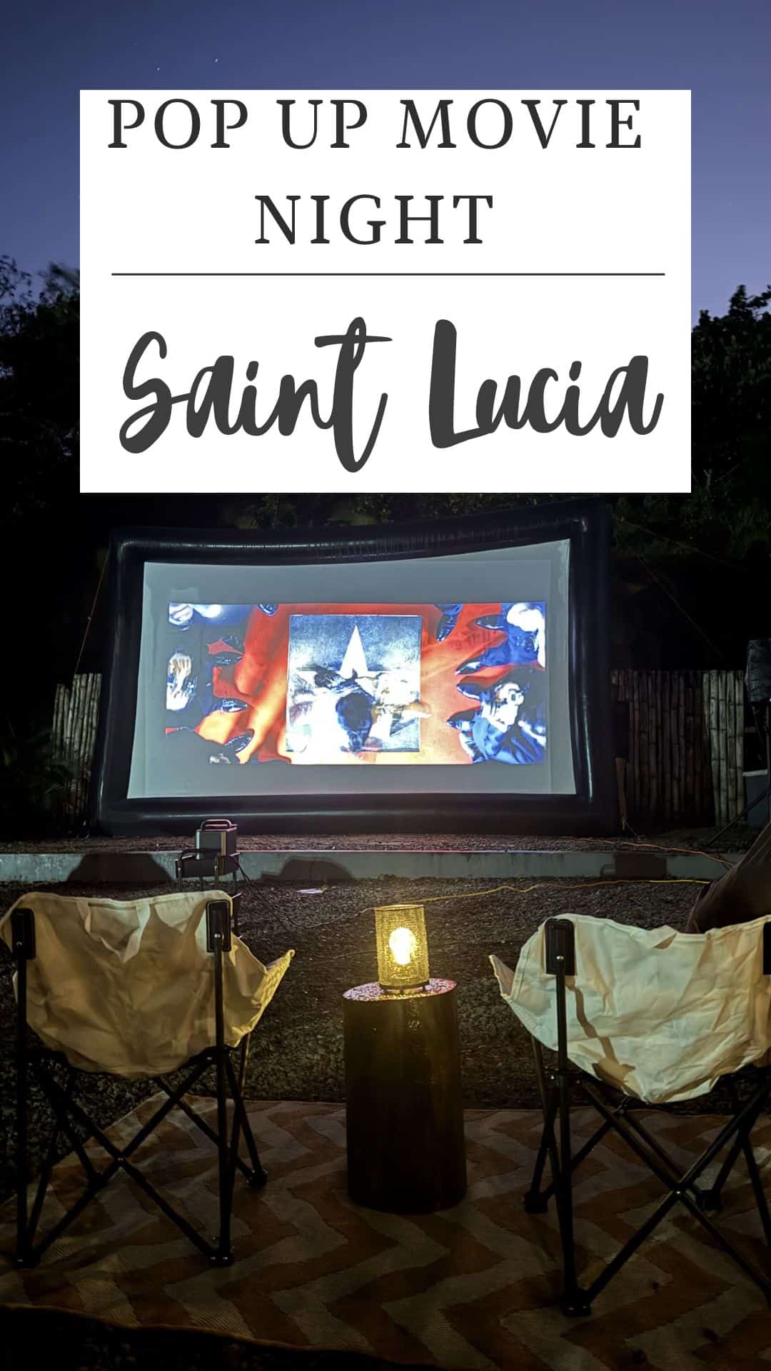Outdoor pop-up cinema setup in Saint Lucia with a large screen playing a film. Two chairs and a lantern add charm to the scene. A sign above reads "Pop Up Movie Night.