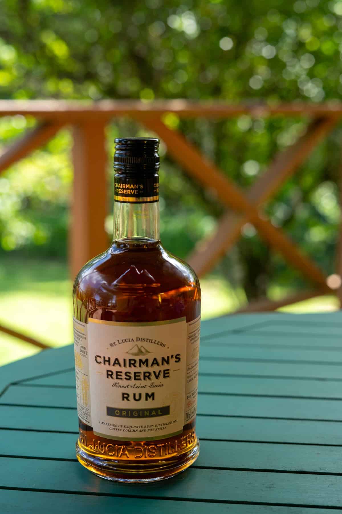 A bottle of Chairman's Reserve Original Saint Lucia Rum sits on a green outdoor table with a blurred garden background.