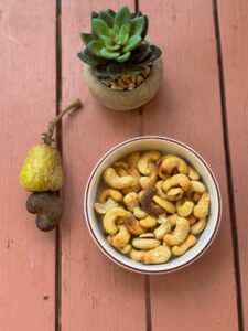 A bowl of roasted cashew nuts, a cashew fruit with attached nut, and a small potted succulent on a wooden surface highlight the unique appeal of cashews in Saint Lucia.