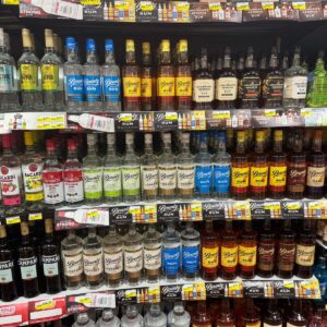 Shelves in a store display various brands and types of rum, including light, dark, and flavored options such as Saint Lucia rum, with price tags visible below each bottle.