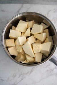 A stainless steel pot containing several large chunks of peeled and cut jackfruit on a marble surface.