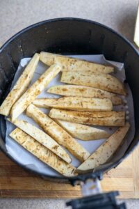 Sliced and seasoned root vegetables, including crispy breadfruit fries, arranged on parchment paper in an air fryer basket, ready to be cooked.