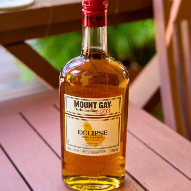A bottle of Mount Gay Eclipse Barbados Rum sits on a pink wooden table, capturing the essence of rum in Barbados against a blurred background.
