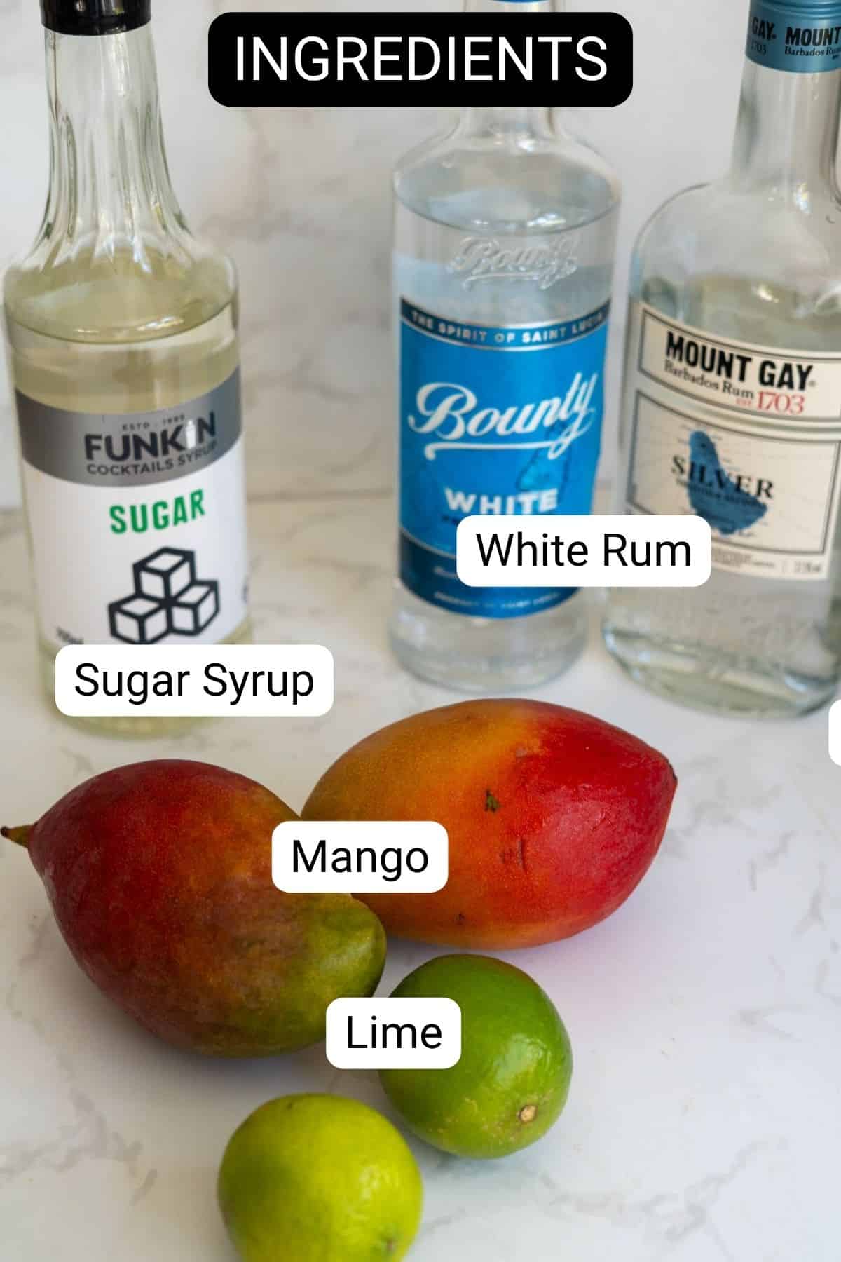 Bottles of sugar syrup, white rum, and silver rum, with a mango and two limes arranged on a white surface, labeled as ingredients.